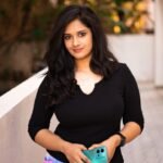 A woman in black stands outdoors holding a green smartphone, exuding confidence.